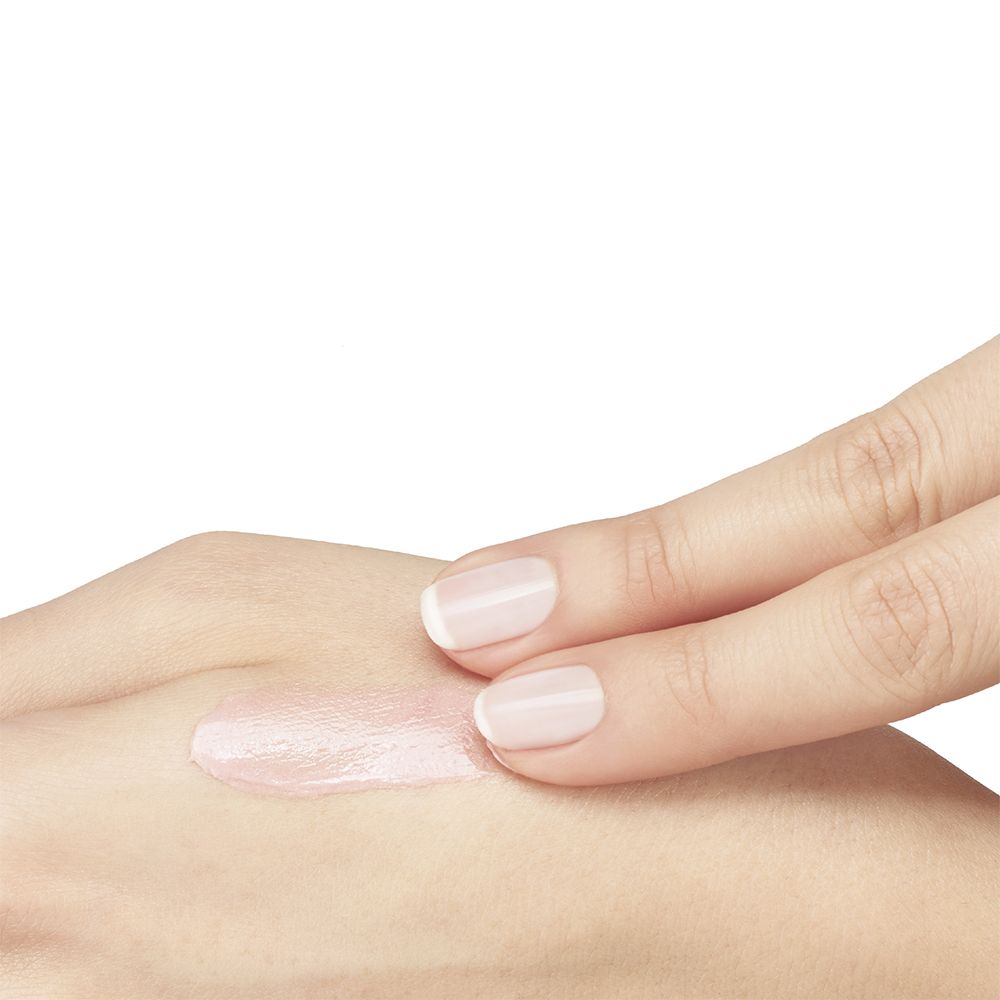 Een hand brengt een kleine hoeveelheid roze oogverzorging aan op de huid.