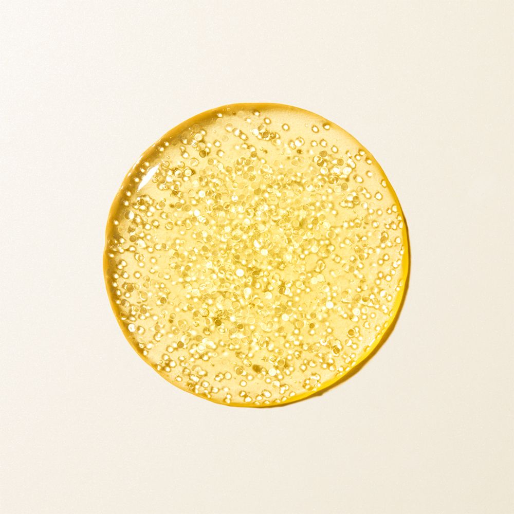 Cirkelvormige druppel gelig serum met gouden deeltjes.