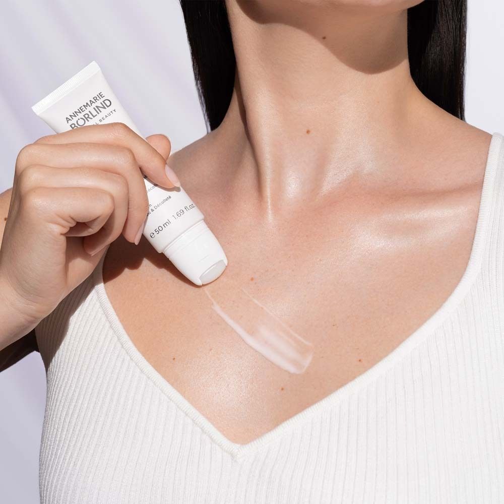Vrouw draagt witte top. Ze houdt een tube vast en brengt serum aan op de hals. Merk: ANNEMARIE BÖRLIND.