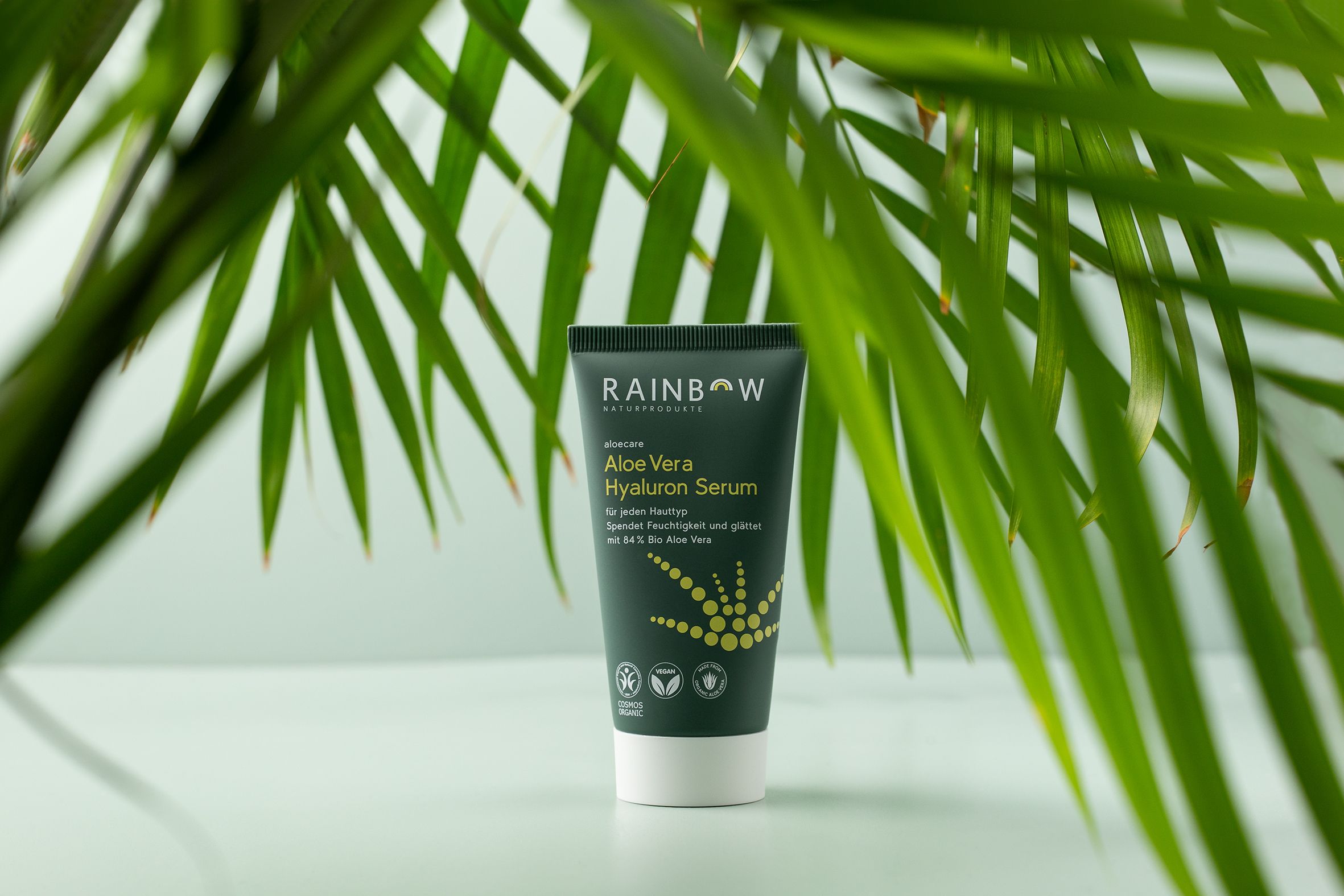 Groene tube voor bladeren. Product: Aloe Vera Hyaluron Serum. Vegan- en bio-keurmerk. Groene achtergrond.