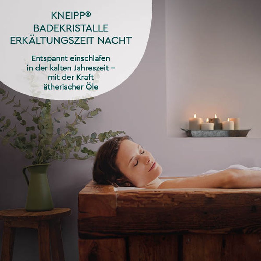Vrouw in een bad. Op de achtergrond kaarsen en een groene vaas. Product: Kneipp® Badekristalle ERKÄLTUNGSZEIT NACHT.