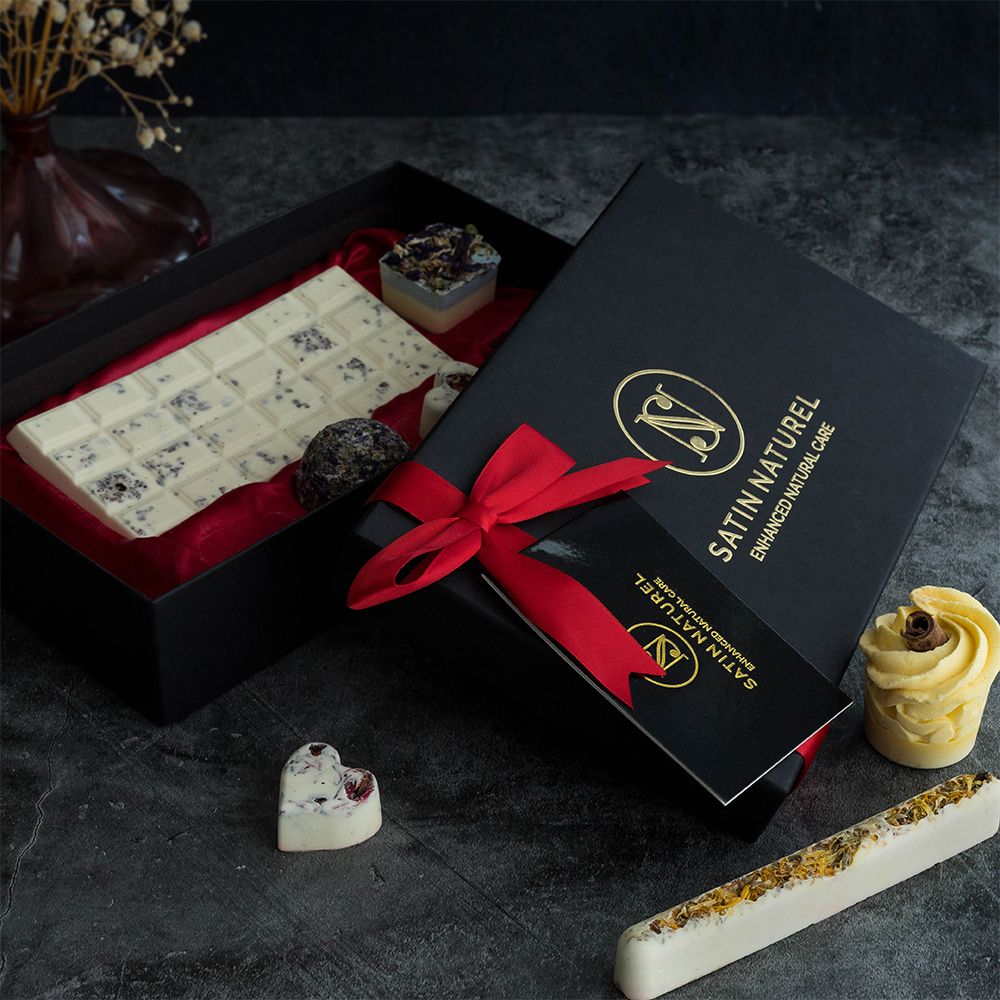Cadeaudoos met badpralines. Zwarte doos met rode strik. Bevat badpralines in verschillende vormen. Logo en tekst op de doos.