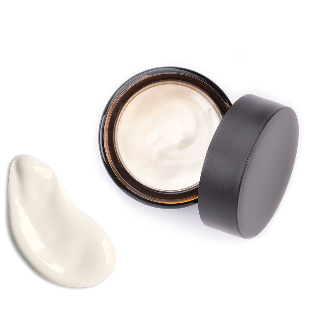 Crèmepot, deksel ernaast. Crèmevlek ernaast. Productnaam op het etiket. Bruin glas.