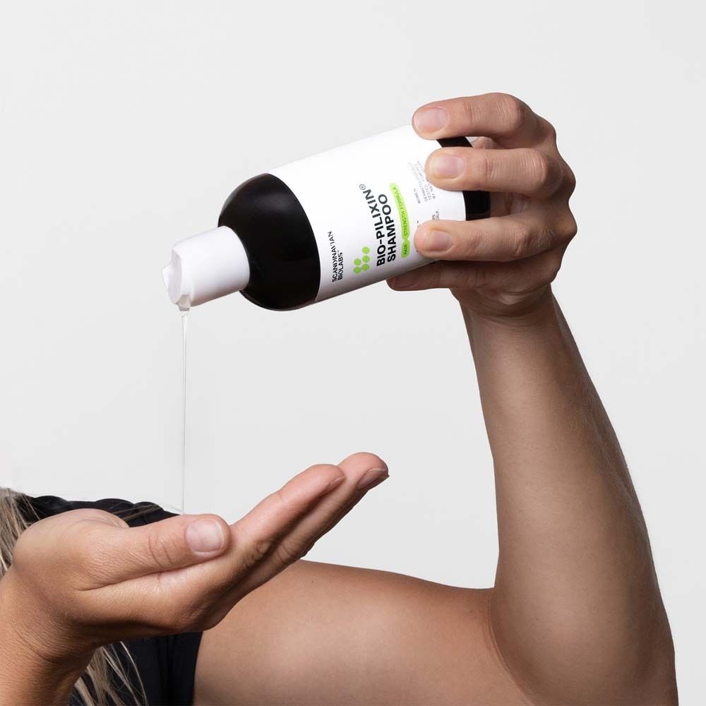 Mains tenant un flacon de shampooing. Liquide s'écoulant de l'ouverture. Inscription : Bio-Pilixin Shampoo.