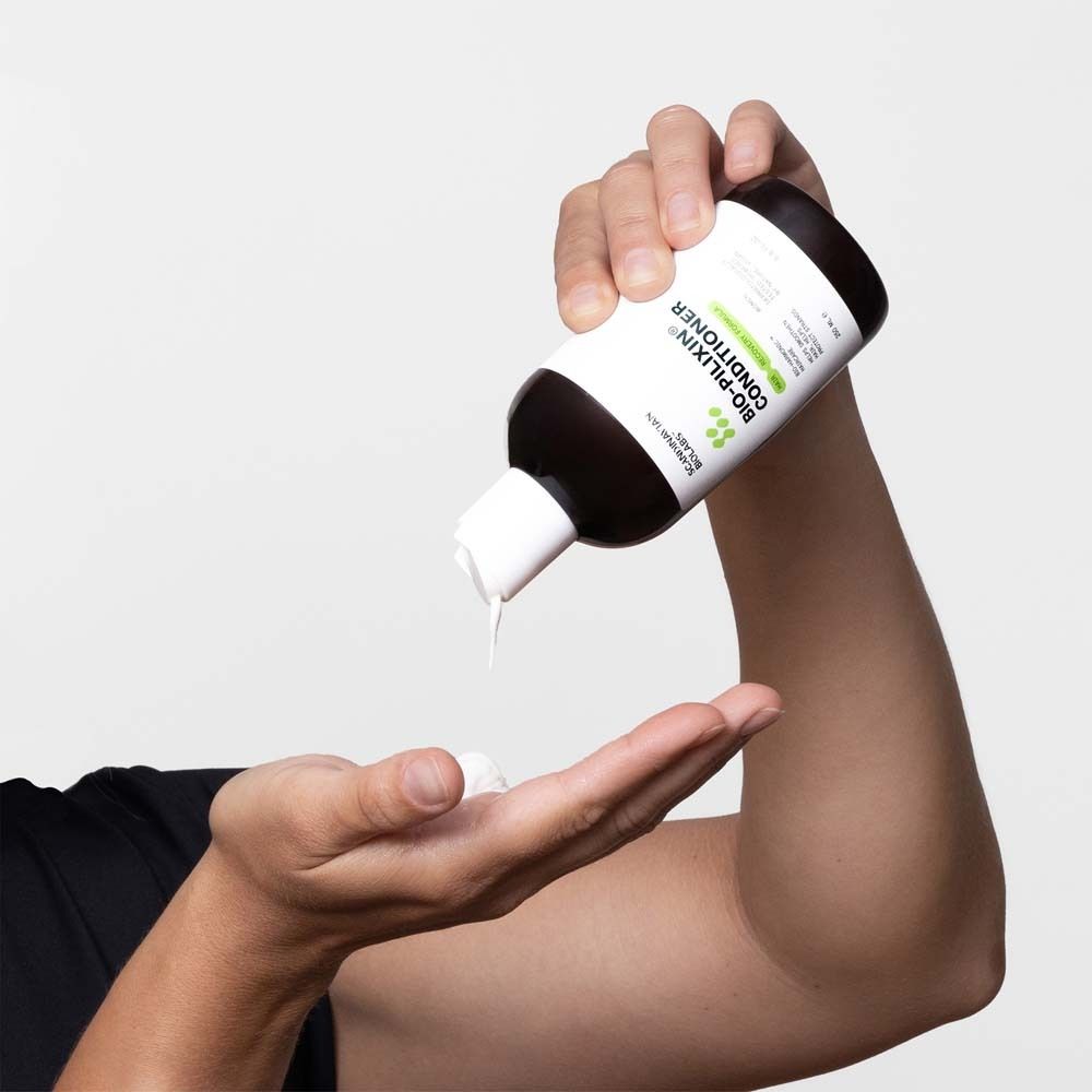 Persoon houdt fles vast en giet conditioner op hand. Product: Bio-Pilixin Conditioner. Witte vloeistof.