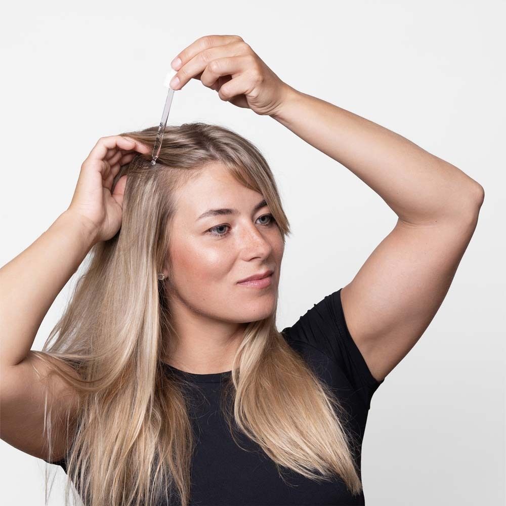 Vrouw met pipet bij haarlijn. Blond haar, zwarte top.