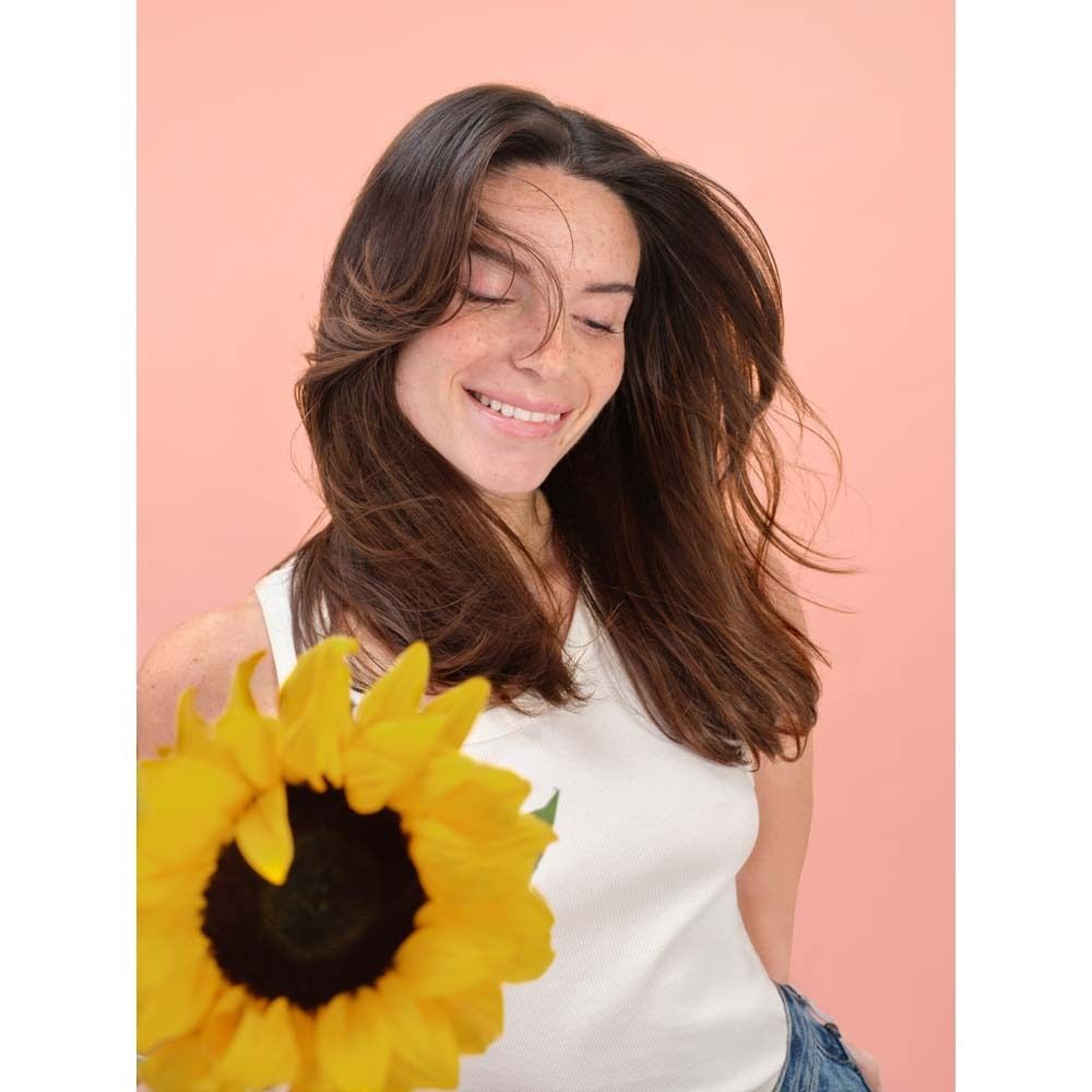 Vrouw met bruin haar en zonnebloem. Ze glimlacht en houdt de bloem voor zich.