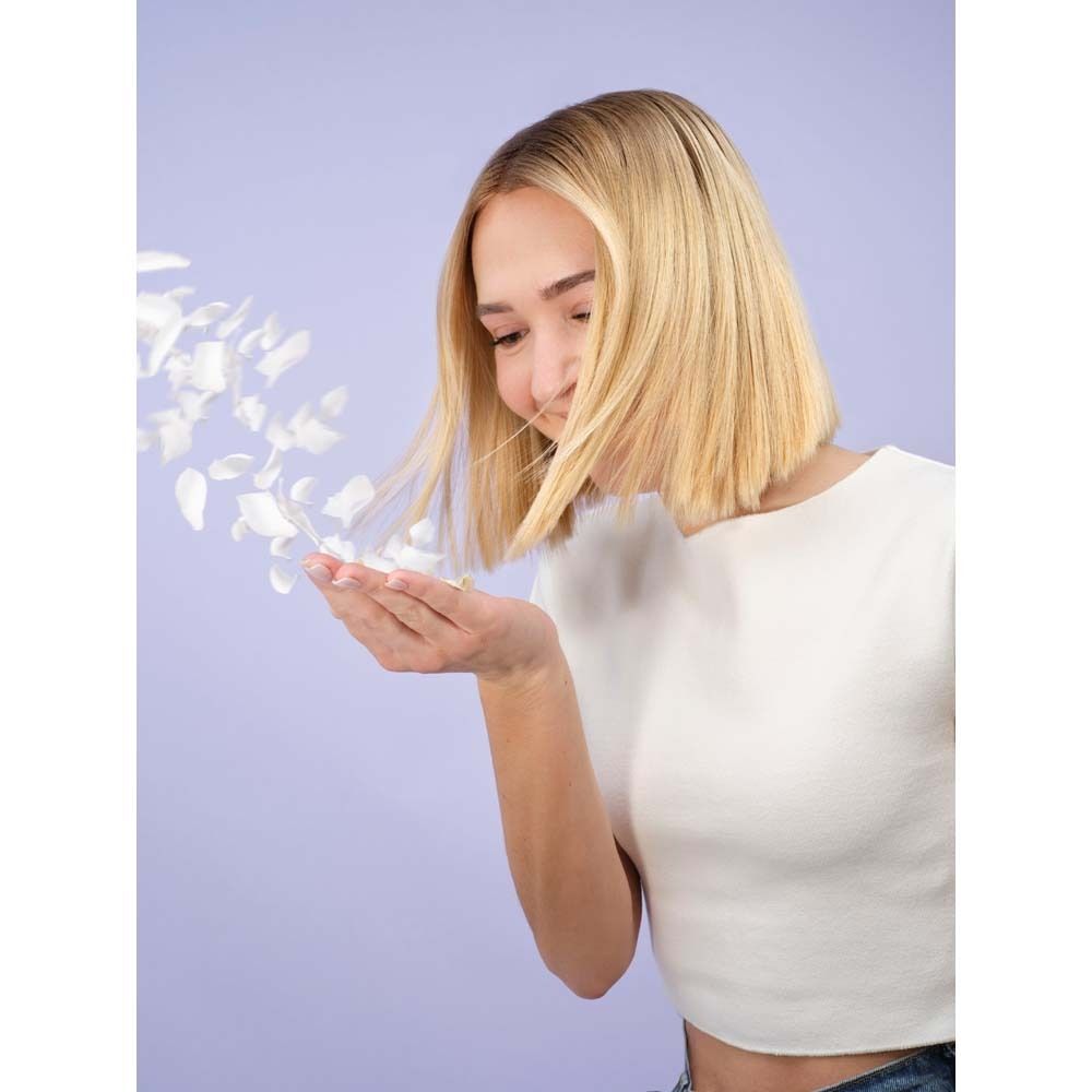 Une femme aux cheveux blonds souffle des pétales blancs de sa paume.