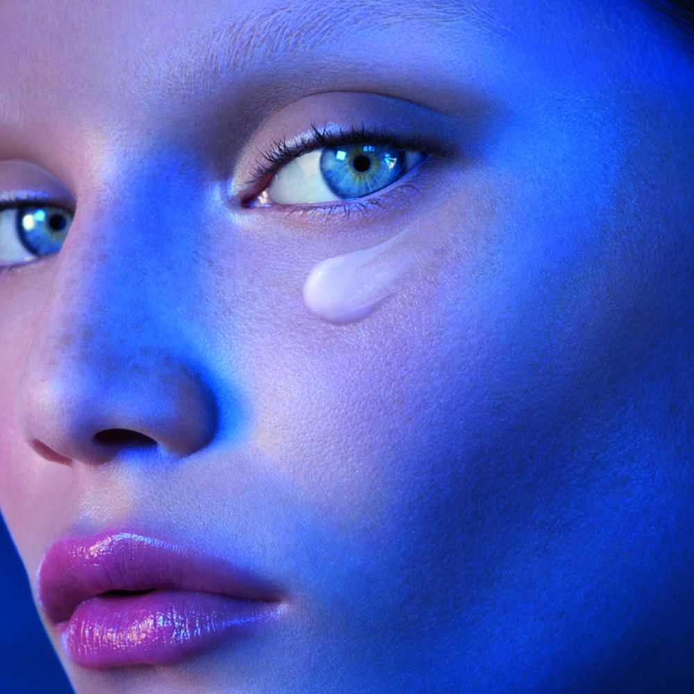 Visage d'une femme. Goutte de crème sous l'œil. Éclairage bleu.