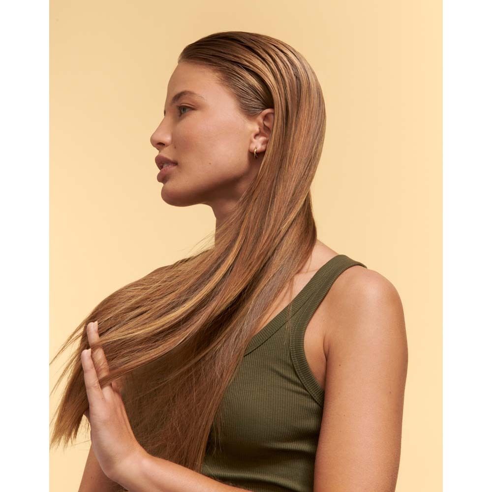 Femme aux longs cheveux brillants touchant ses cheveux.
