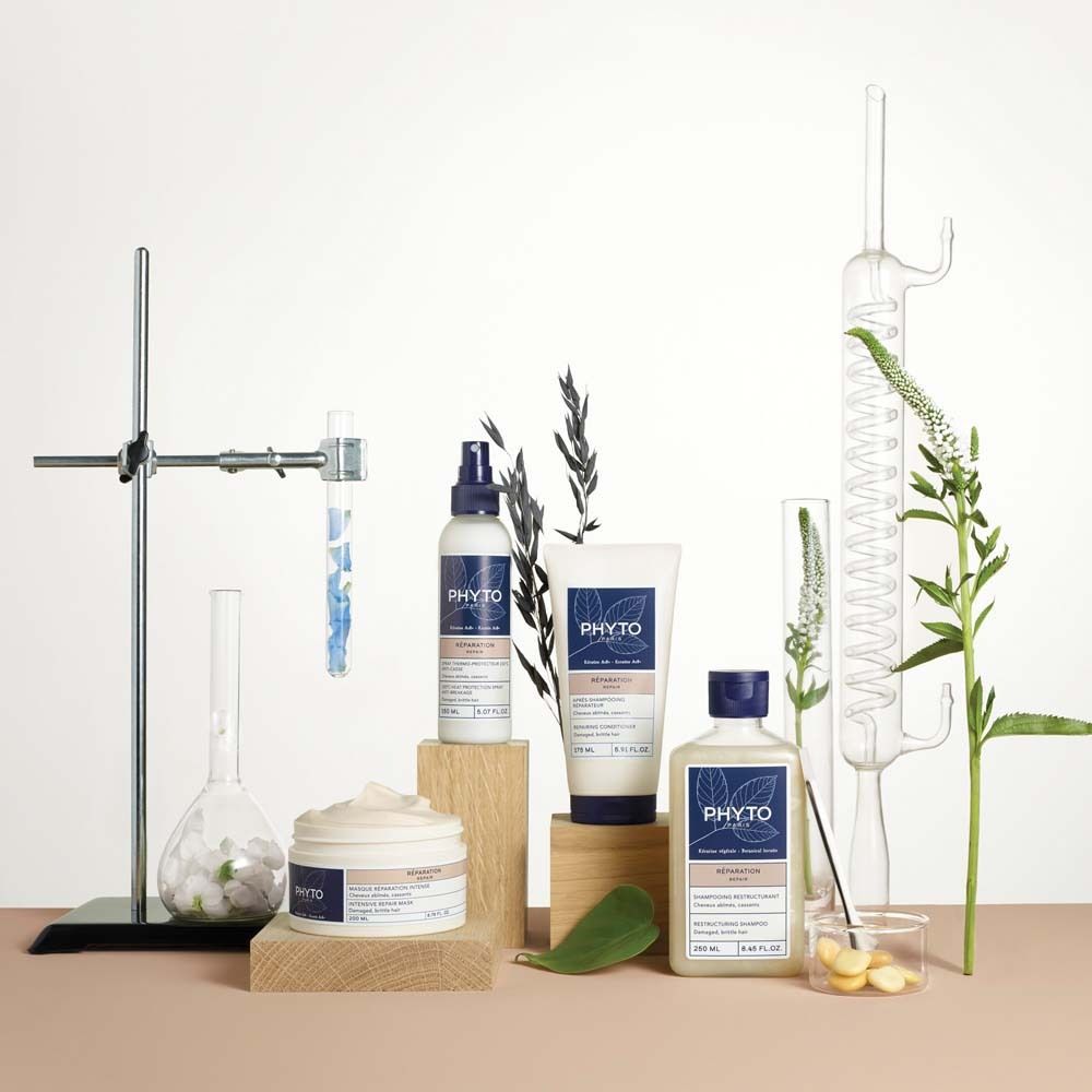 Trois produits capillaires Phyto : une crème, un spray et une bouteille de shampoing, disposés avec du matériel de laboratoire et des plantes.