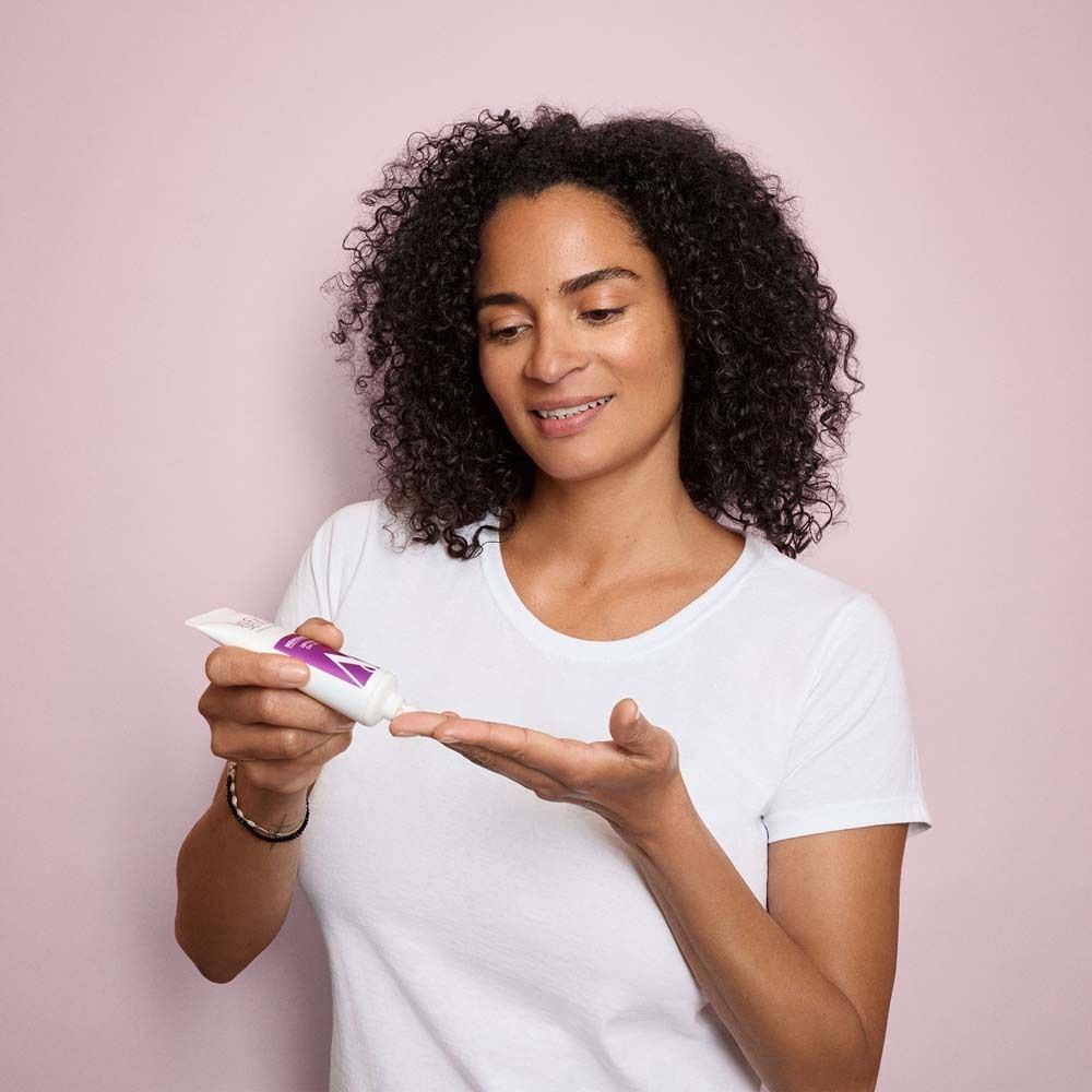 Vrouw met krullen houdt tube vast. Crème op handpalm. Roze achtergrond.