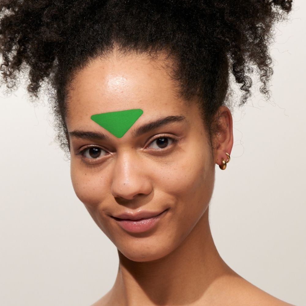 Une femme avec un patch triangulaire vert sur le front. Boucles d'oreilles dorées.