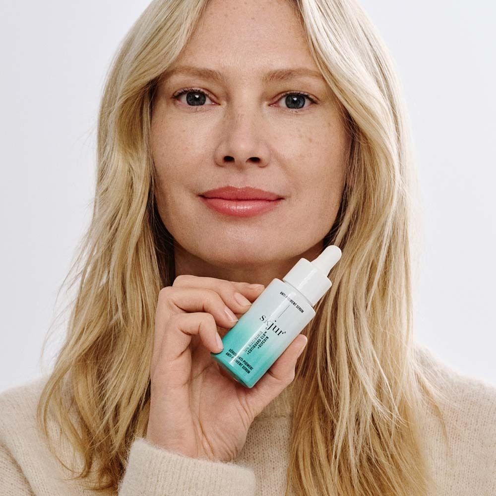 Femme tenant le sérum anti-pigmentaire skjur®. Flacon avec pipette. Cheveux blonds.