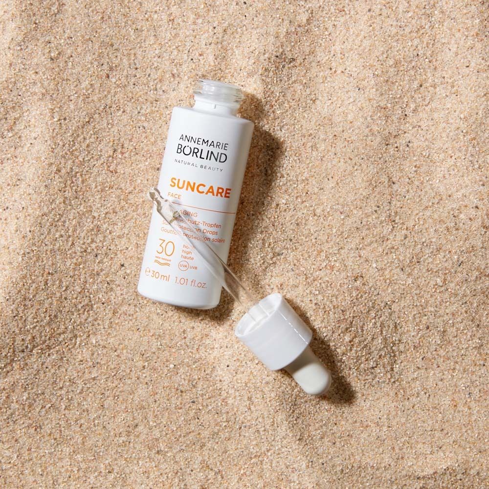 Witte fles met pipet op zand. Opschrift: Suncare Face, Anti-Aging, SPF 30.