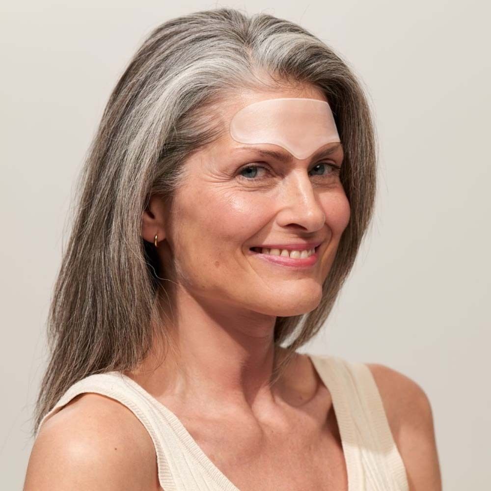 Femme avec Forehead Pad sur le front. Pad transparent. Cheveux gris. Haut beige.