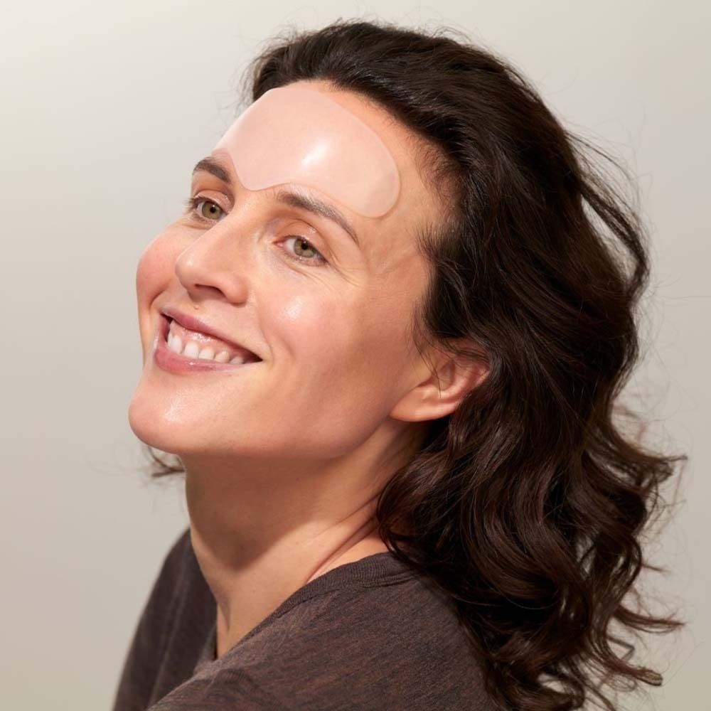 Vrouw met voorhoofdpad op het voorhoofd. Transparant pad. Vrouw lacht. Bruin haar, bruine top.