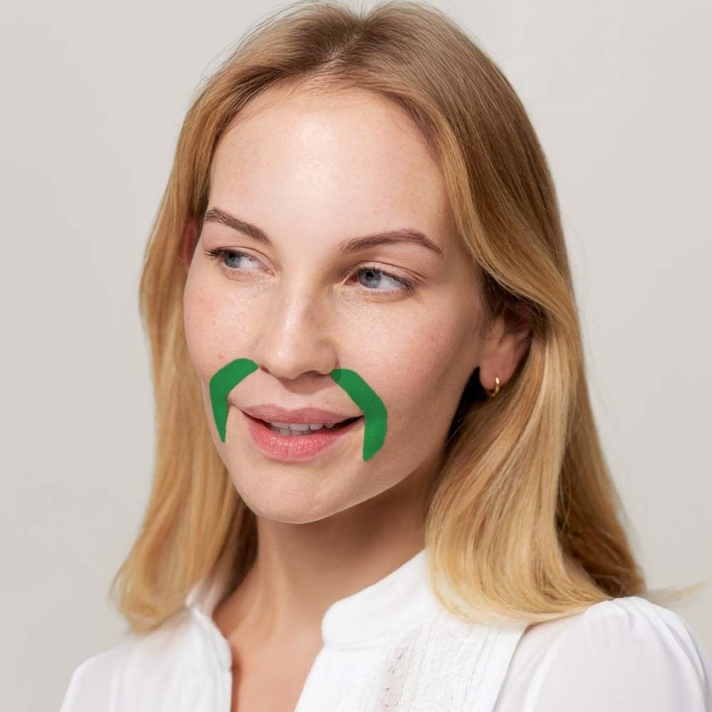 Femme blonde avec des patchs buccaux verts. Elle sourit.