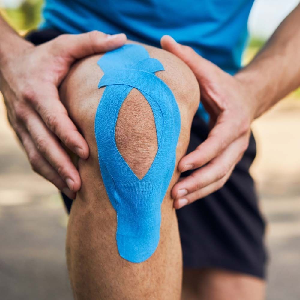Knie met blauwe kinesiotape. Handen houden de knie vast.