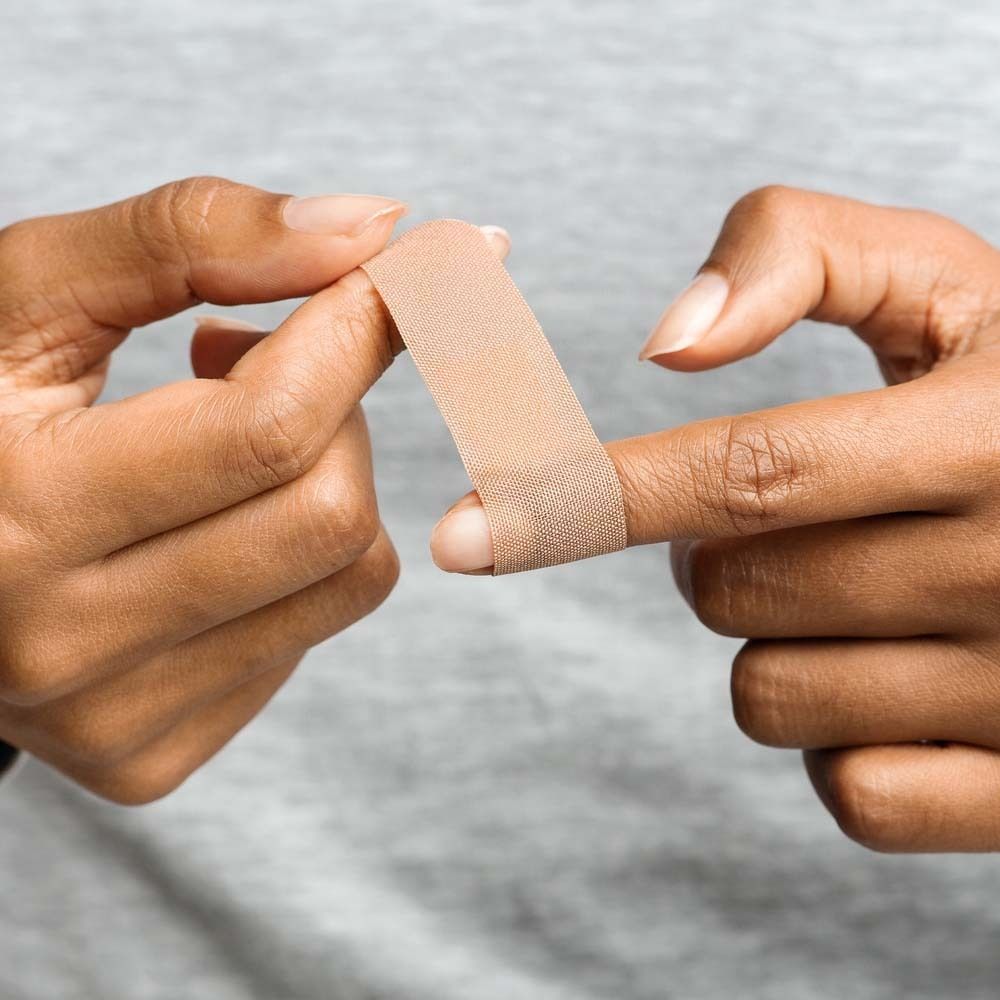 Handen plakken vingerpleister. Beige pleister op vinger. Grijze achtergrond.