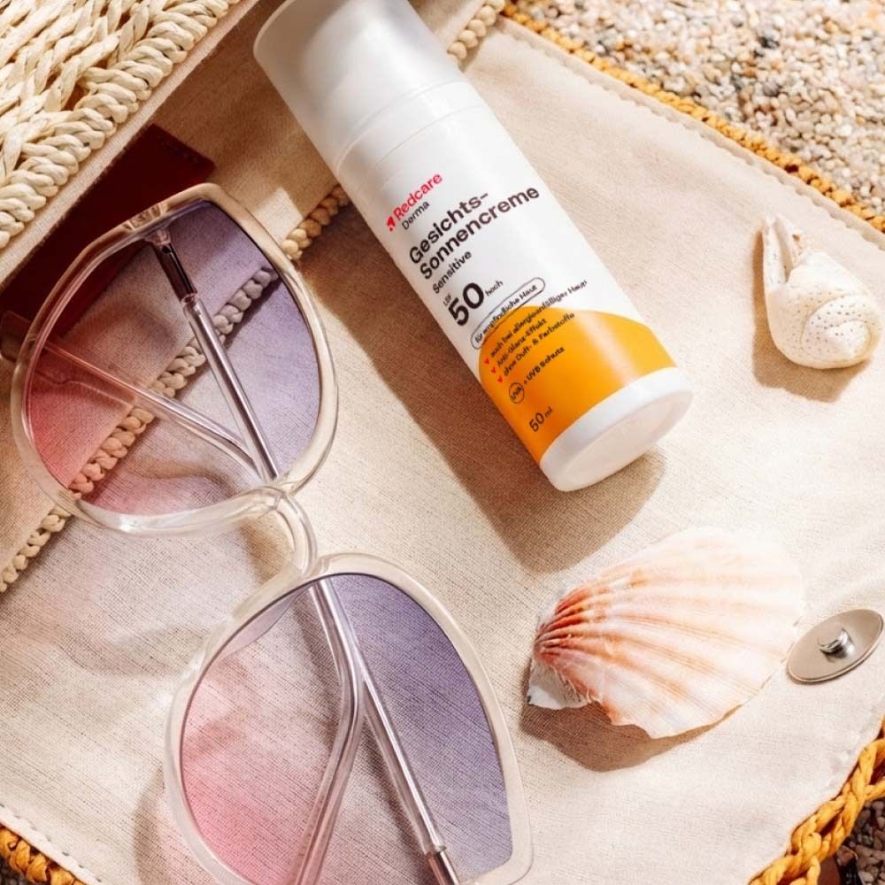 Zonnecrèmefles, zonnebril en schelp op een strandtas. Strandachtergrond.