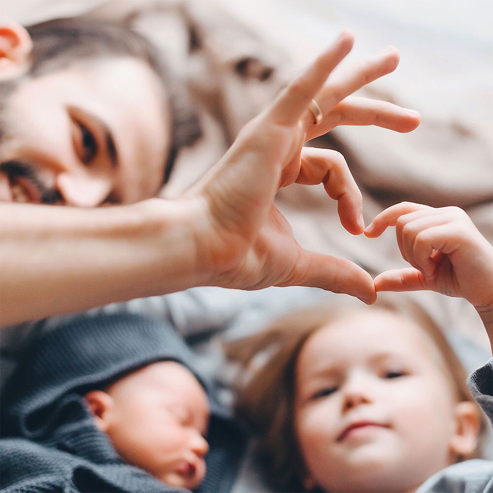 Famille allongée dans un lit. Mains formant un cœur. Bébé et jeune enfant.