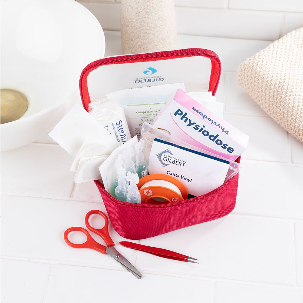 Open rode EHBO-tas met inhoud. Schaar, pincet, verband, handschoenen, pleister, serum. Achtergrond: wastafel.