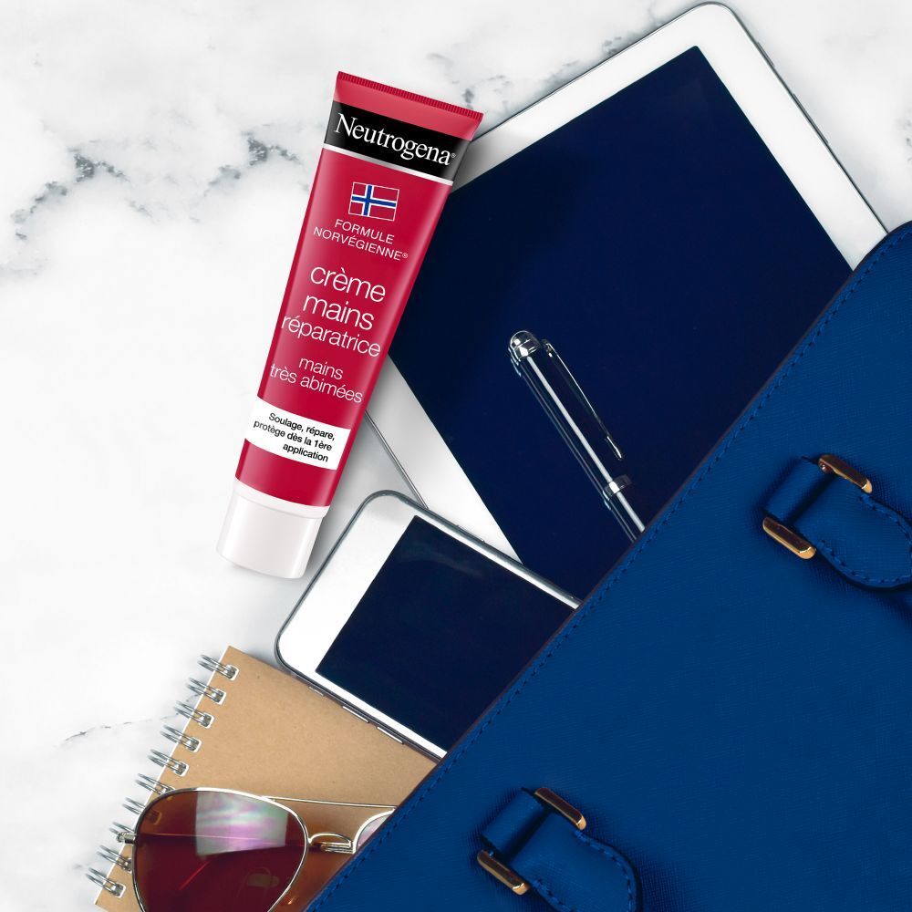 Handcrèmetube naast tablet, telefoon, bril en notitieboek in tas.