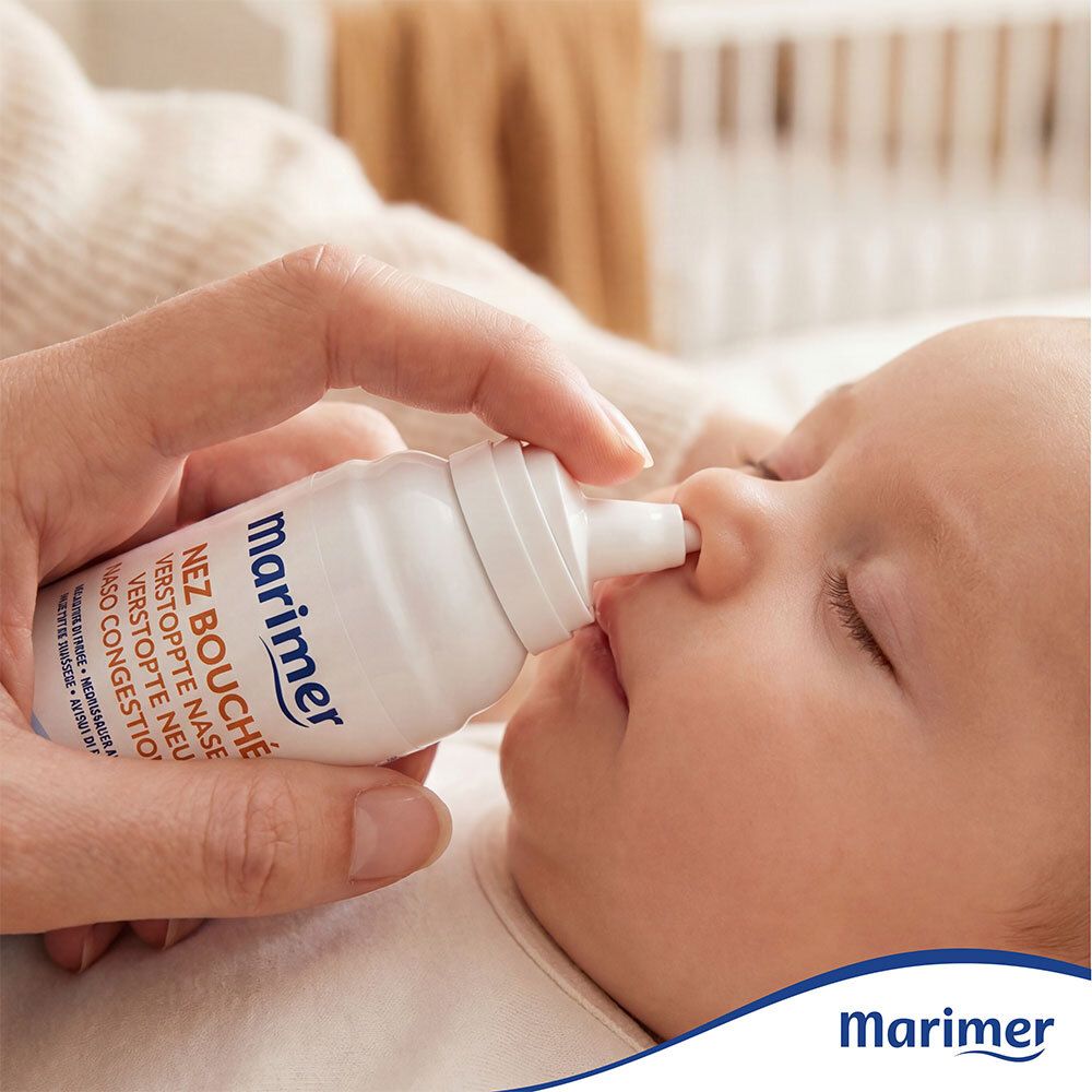 Baby krijgt neusspray. Marimer Baby Nez Bouché fles. Persoon houdt flesje tegen baby's neus.