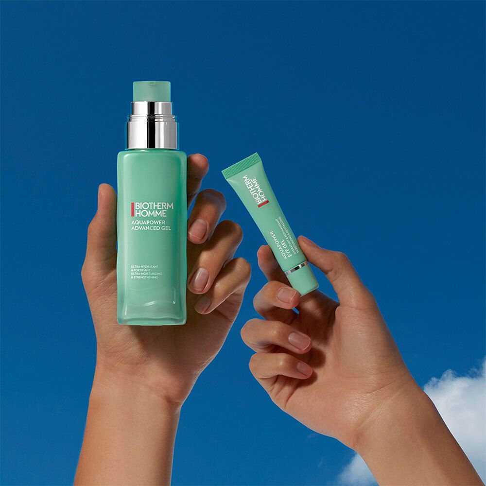 Handen houden een fles en een tube vast. Fles: BIOTHERM HOMME, AQUAPOWER. Tube: BIOTHERM HOMME, AQUAPOWER EYE GEL. Blauwe lucht op de achtergrond.