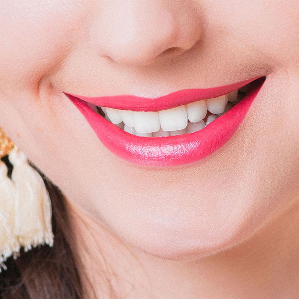 Close-up van een lachende mond met roze lipstick. Witte tanden zichtbaar.