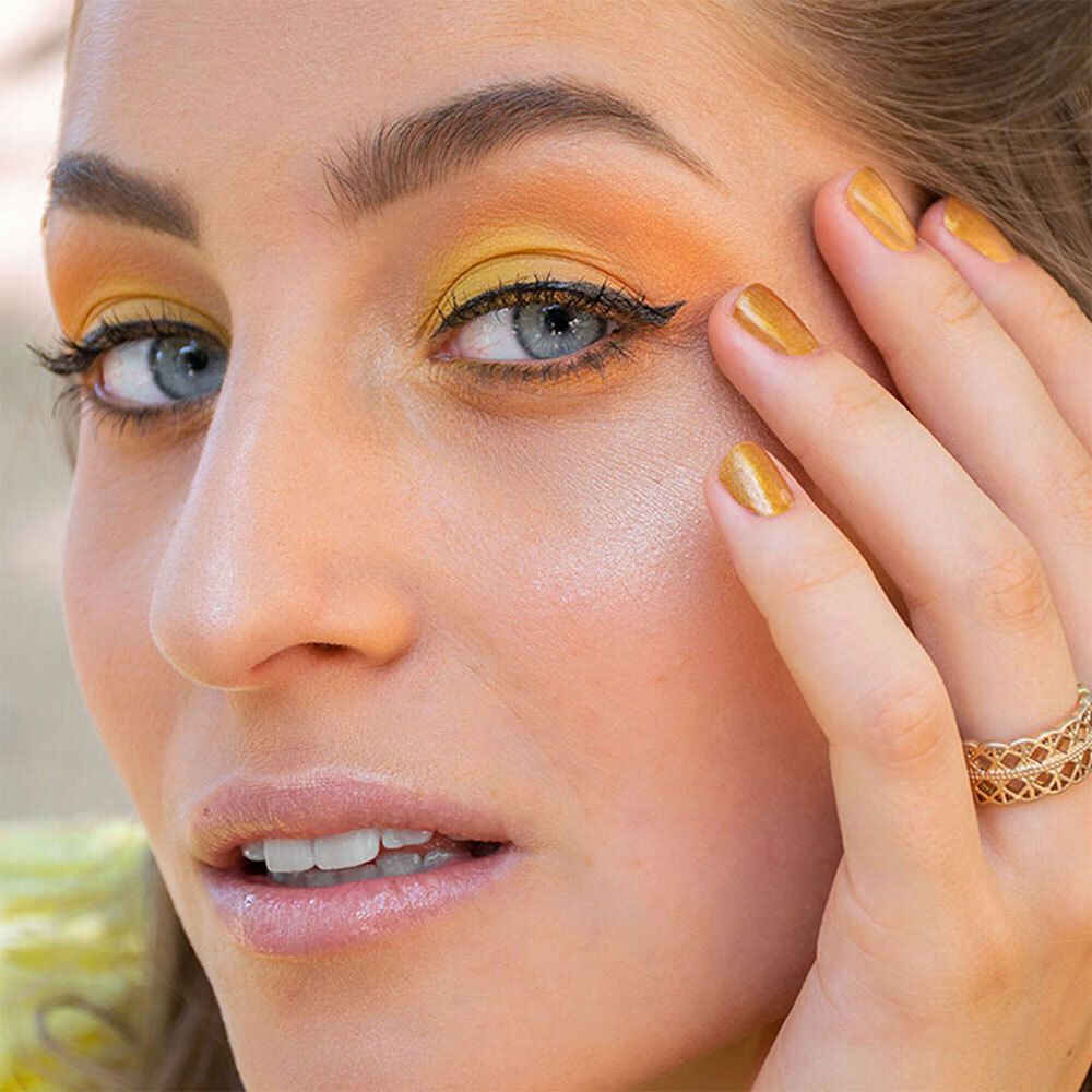 Gros plan d'une femme avec fard à paupières jaune et eyeliner noir. Bague dorée au doigt.