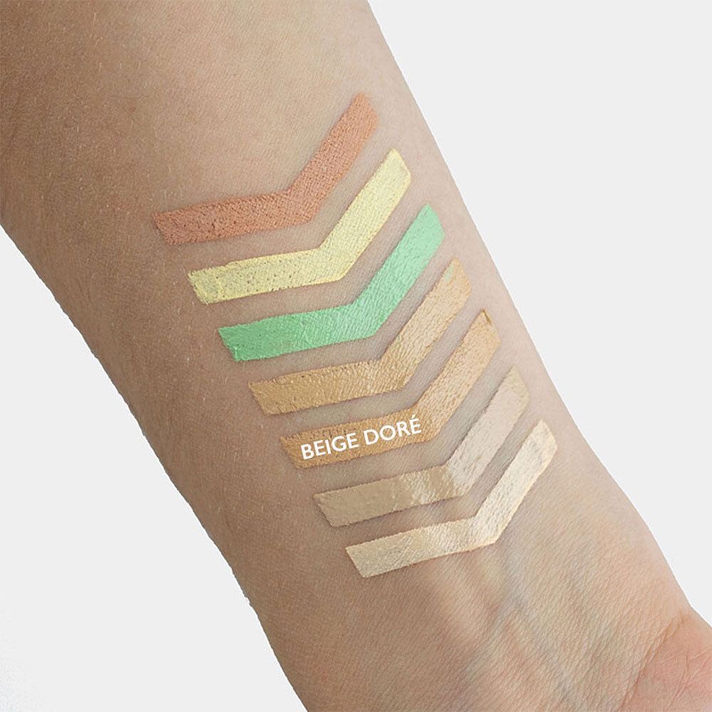 Arm met kleurstalen van concealers. Pijlvormige kleurvlakken in verschillende tinten. Tekst: BEIGE DORÉ.