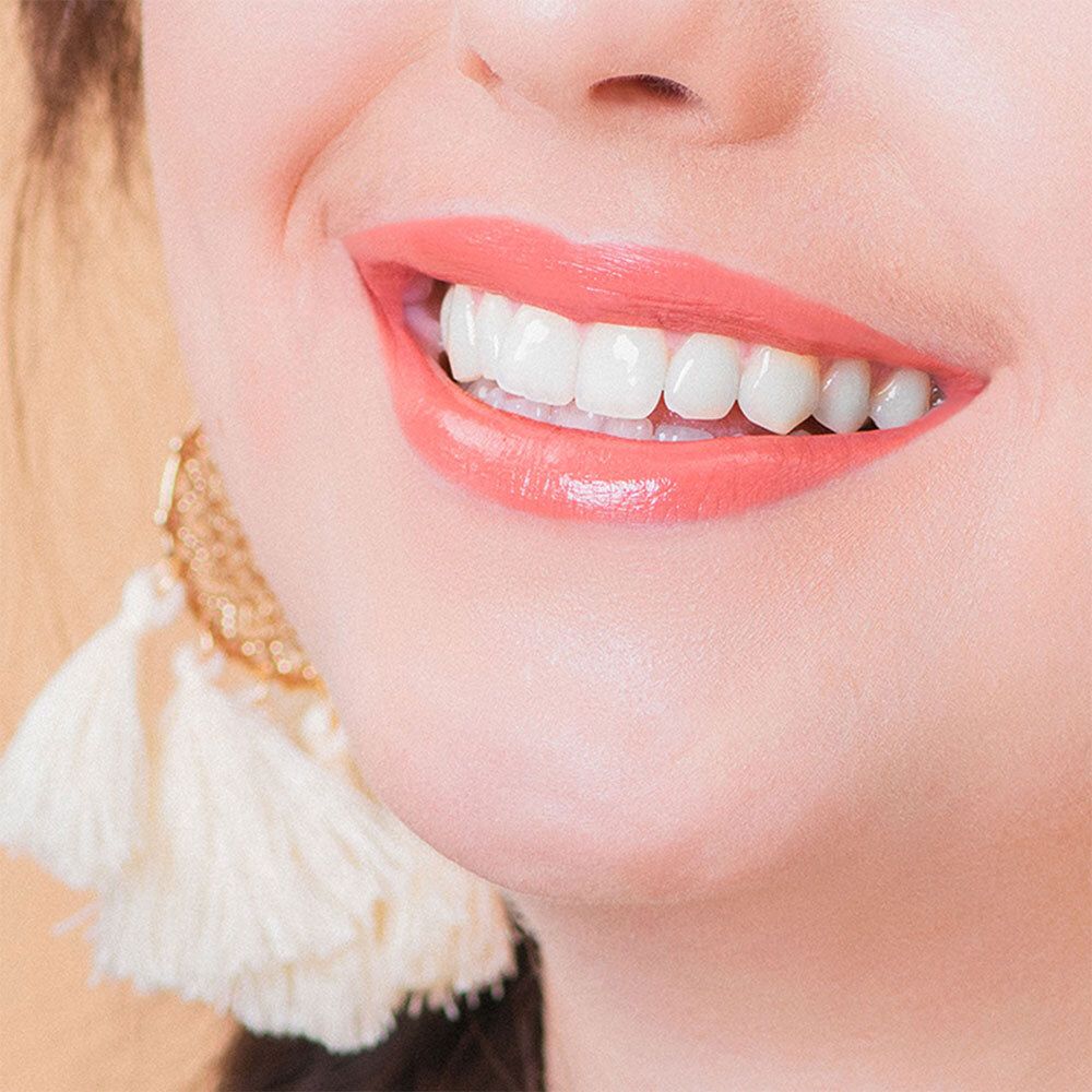 Gros plan d'un sourire avec rouge à lèvres rose. Dents et lèvres visibles. Boucle d'oreille avec glands.