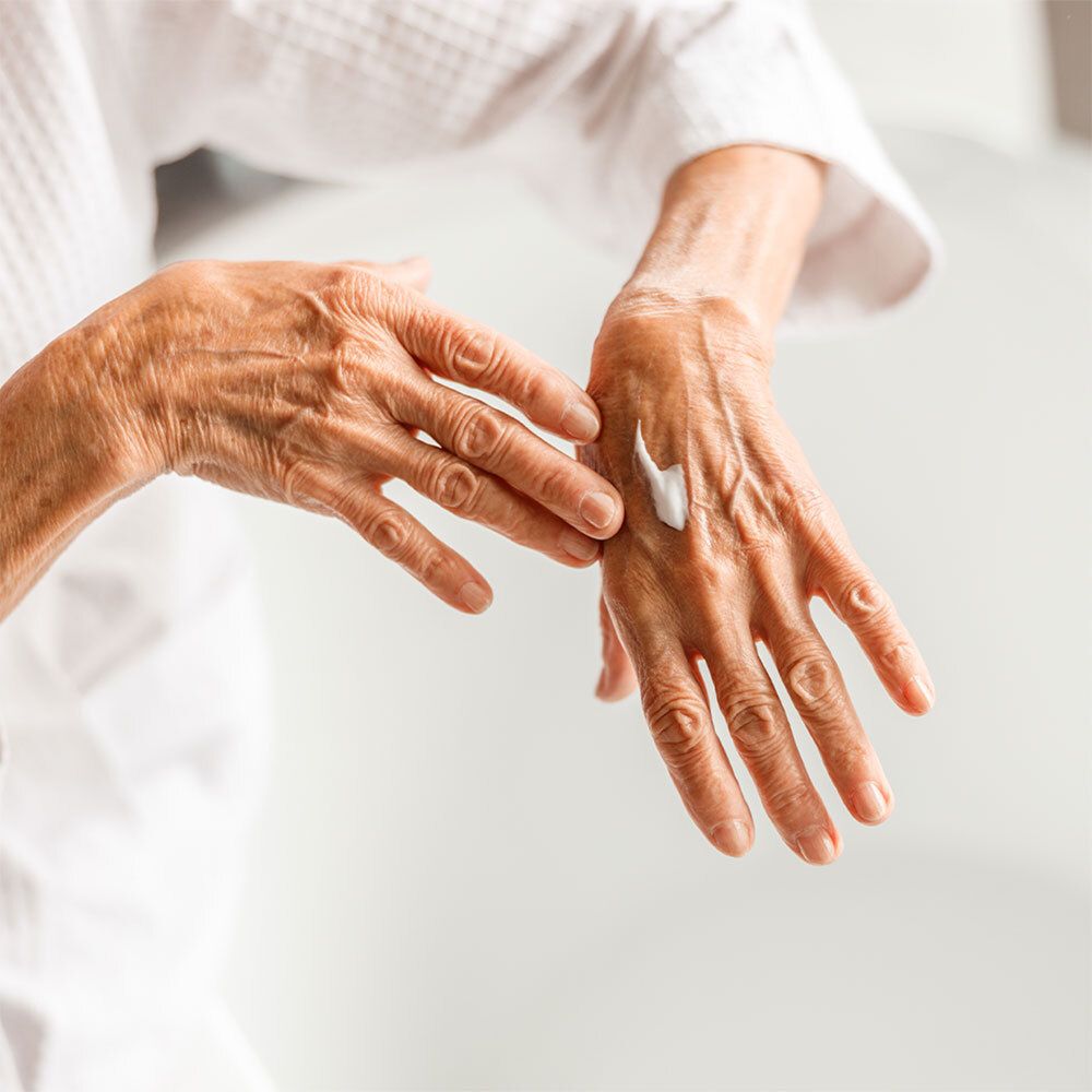Oudere handen die crème aanbrengen. Een kleine hoeveelheid crème op de handpalm. Persoon draagt een witte badjas.