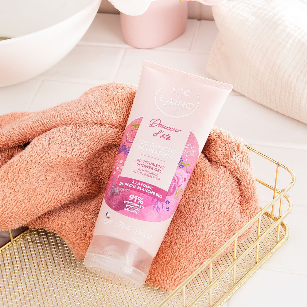 Roze tube LAINO "Gel Douche Hydratant" op een handdoek en in een mand. Achtergrond: badkamer.