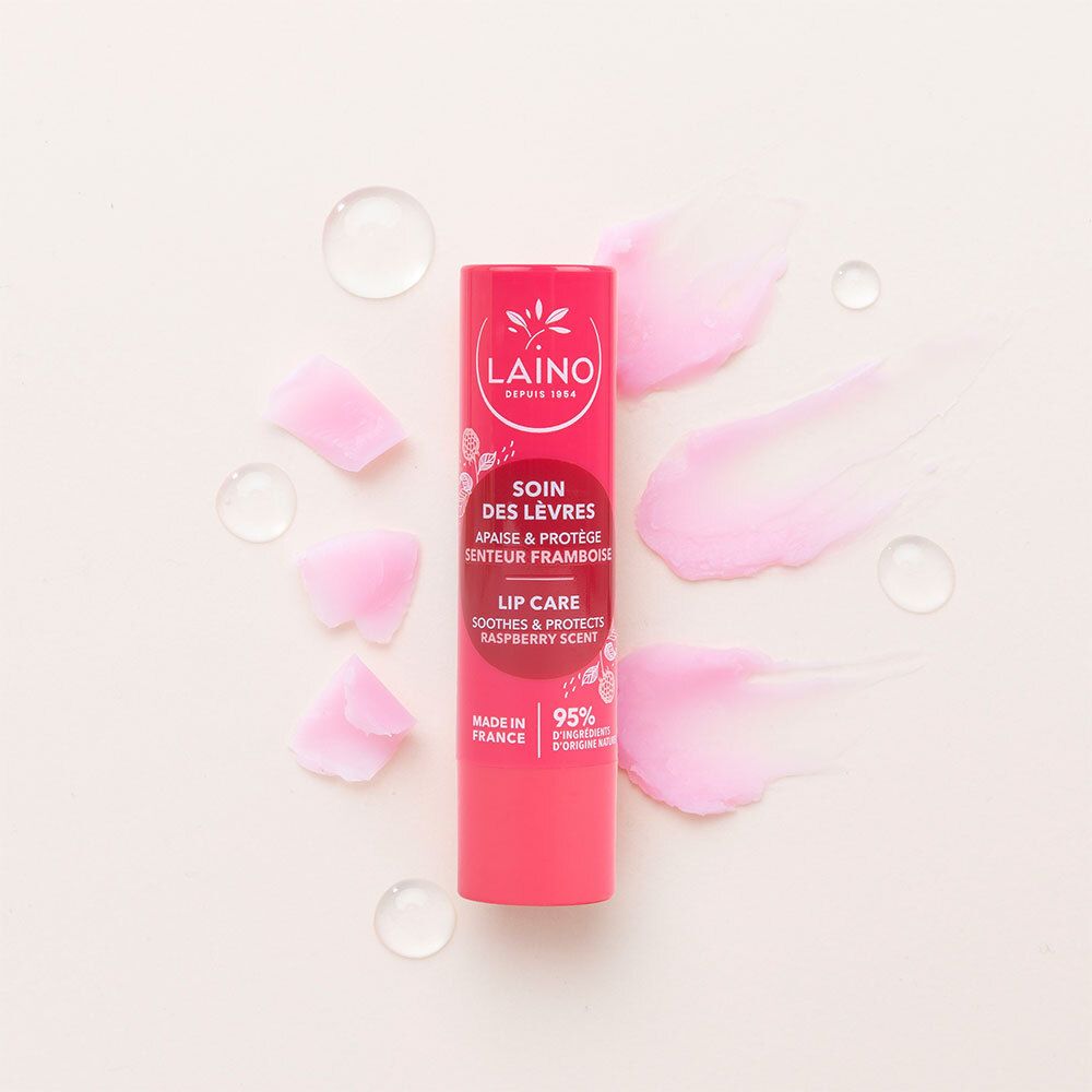 Stick de soin des lèvres rouge avec texte, entouré de pétales roses et gouttes d'eau. Logo LAINO, « Soin des lèvres », parfum framboise, 95% naturel.