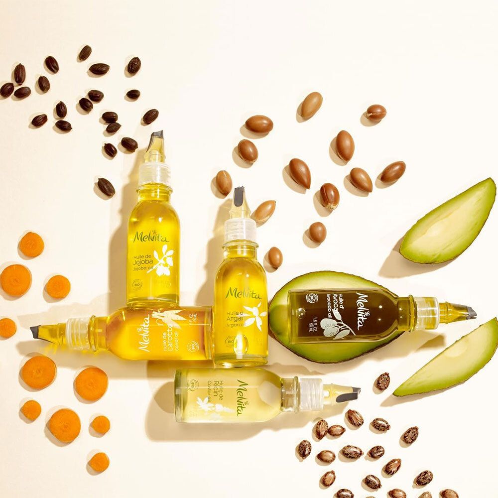 Verschillende flessen met gele vloeistof, omringd door zaden en fruit. Opschrift Melvita.