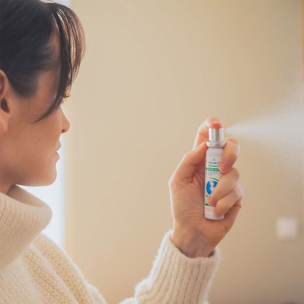 Personne tenant un spray Puresseentiel Resp'OK®. Spray blanc, bouchon vert, brume visible.