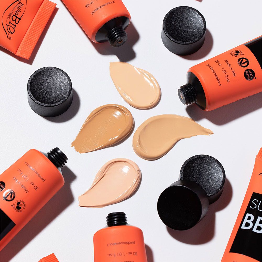 Meerdere tubes en kleurmonsters van BB cream. Oranje tubes met zwarte dop. Kleuren: licht, medium, donker.