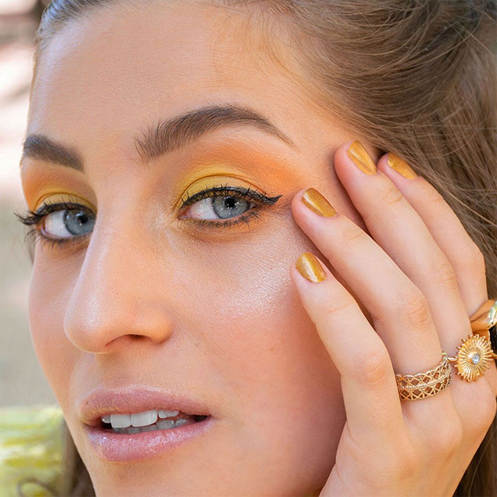 Femme maquillée. Fard à paupières jaune, eye-liner noir, bagues dorées.
