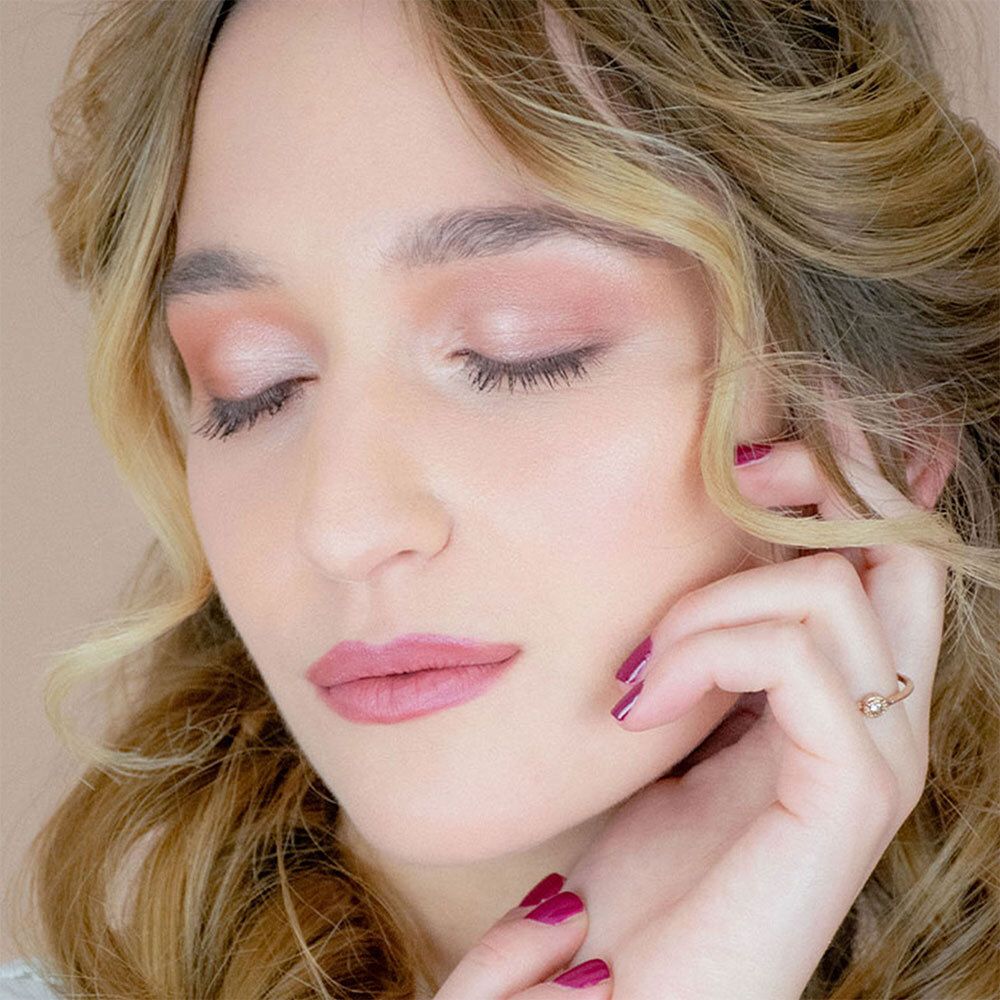 Portrait d'une femme aux yeux fermés. Elle porte de l'ombre à paupières et du rouge à lèvres roses. Sa main touche son visage.