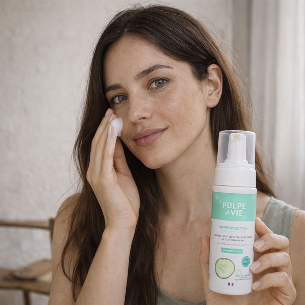 Femme tenant un flacon et nettoyant son visage avec un coton. Nom du produit et logo visibles.