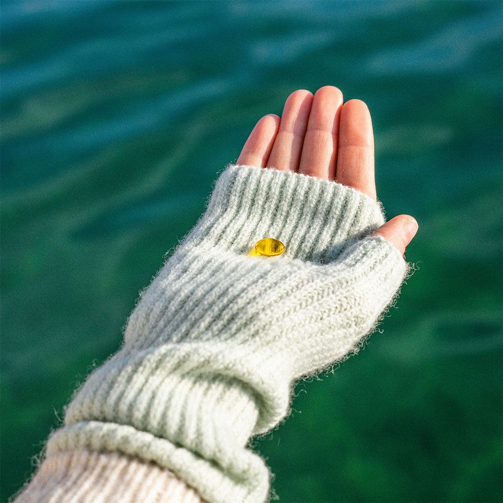 Hand met een gele pastille in een grijze handschoen. Achtergrond: water.