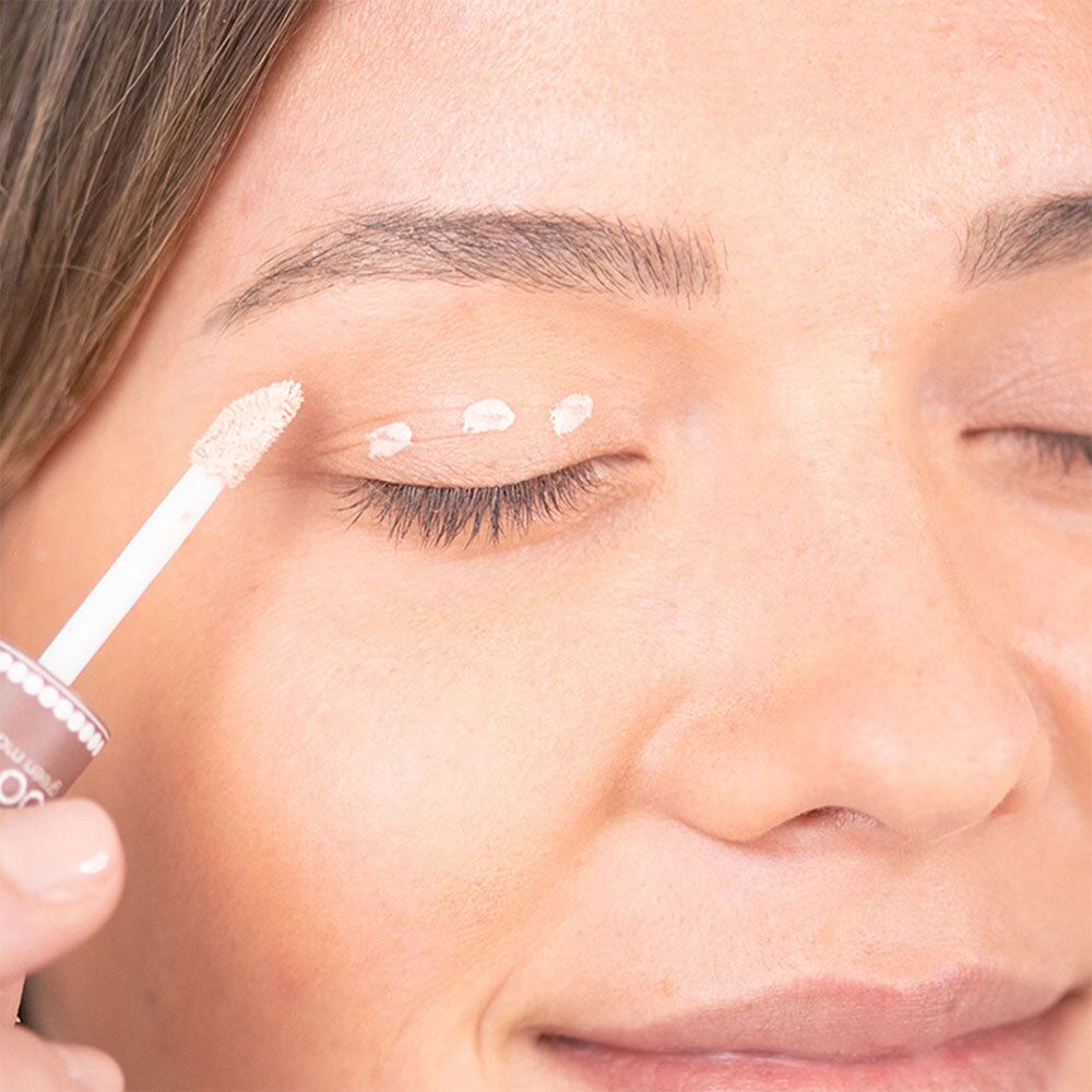 Close-up van een vrouw die een beige oogschaduwbasis op haar ooglid aanbrengt met een applicator.