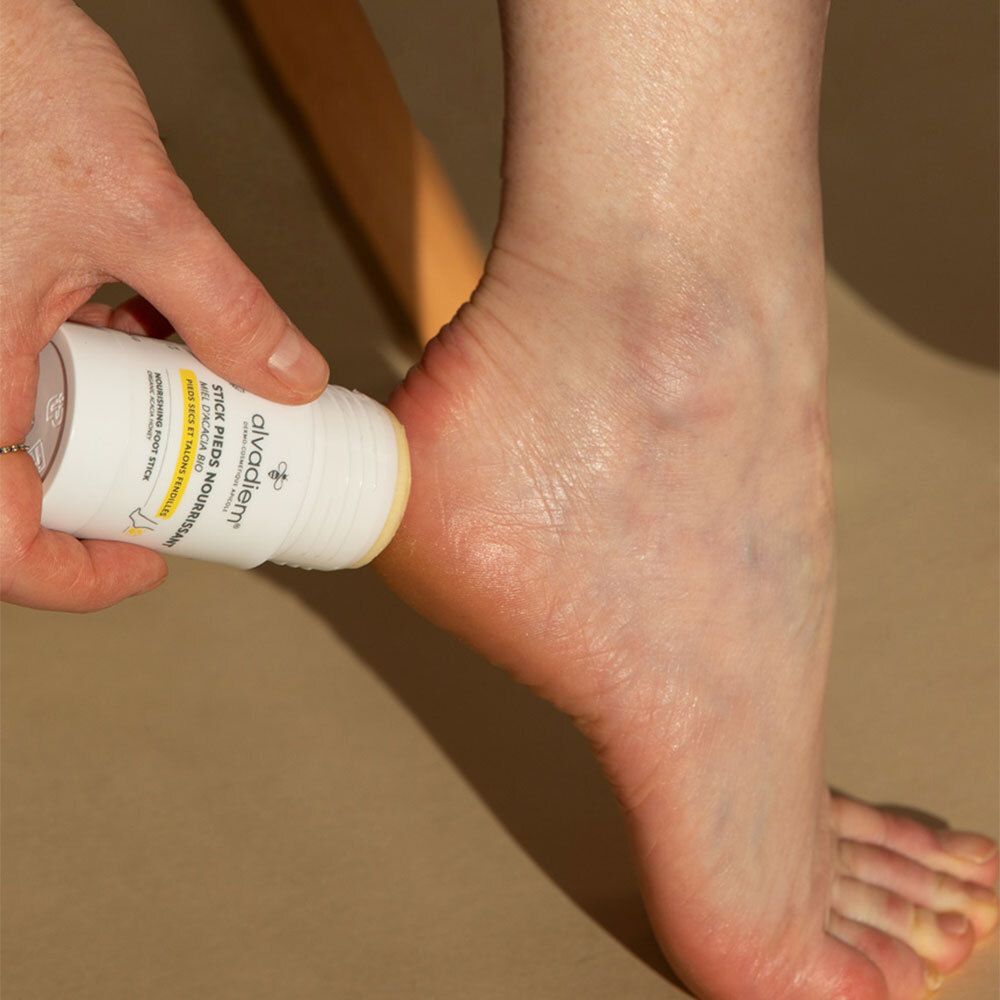 Personne appliquant un stick blanc sur le pied. Inscription: ALVADIEM, STICK PIEDS NOURRISSANT.