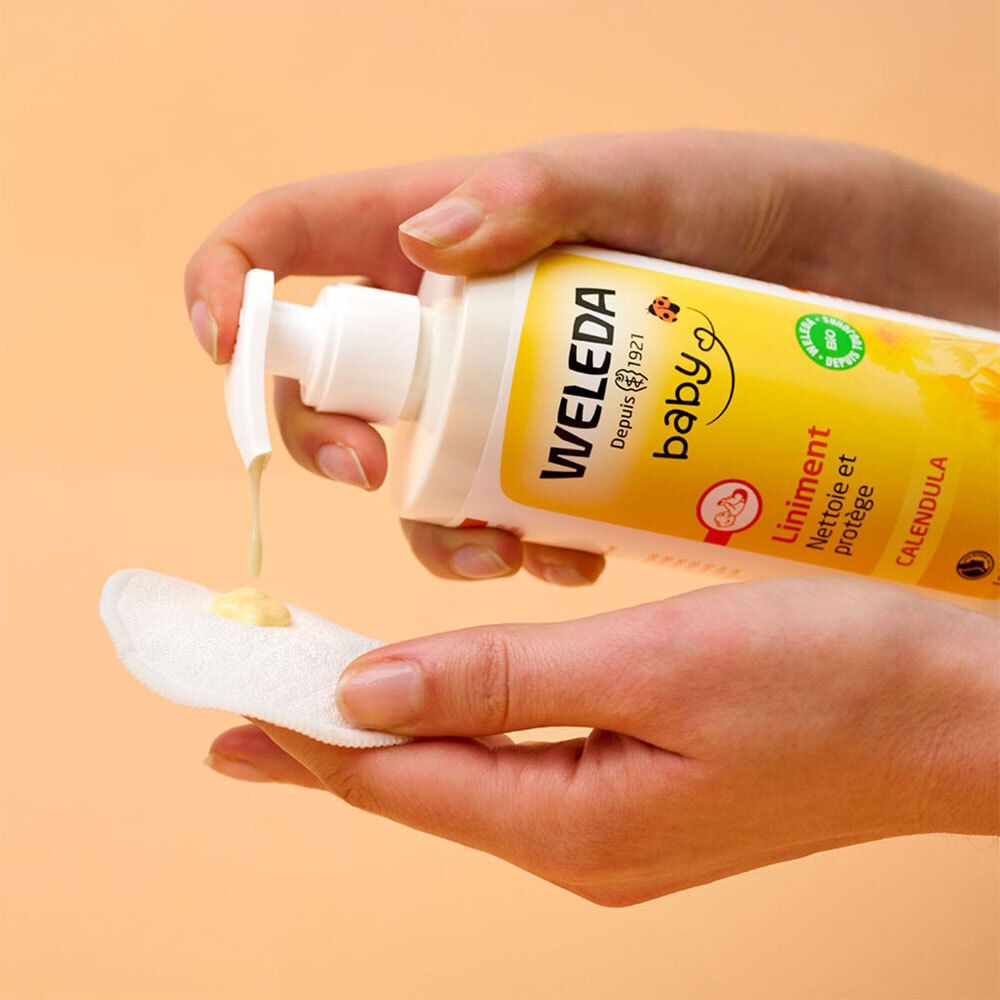 Handen houden een fles WELEDA Baby Liniment vast en gieten vloeistof op een wattenschijfje.