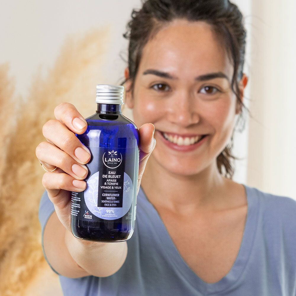 Vrouw houdt LAINO Eau de Bleuet fles vast. Blauwe fles met zilveren dop. Opschrift: Eau de Bleuet, Cornflower Water.