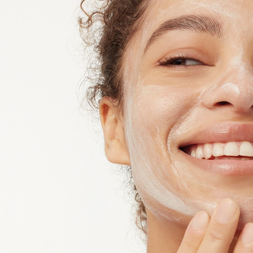 Gros plan d'une personne avec de la mousse blanche sur le visage. La personne sourit.