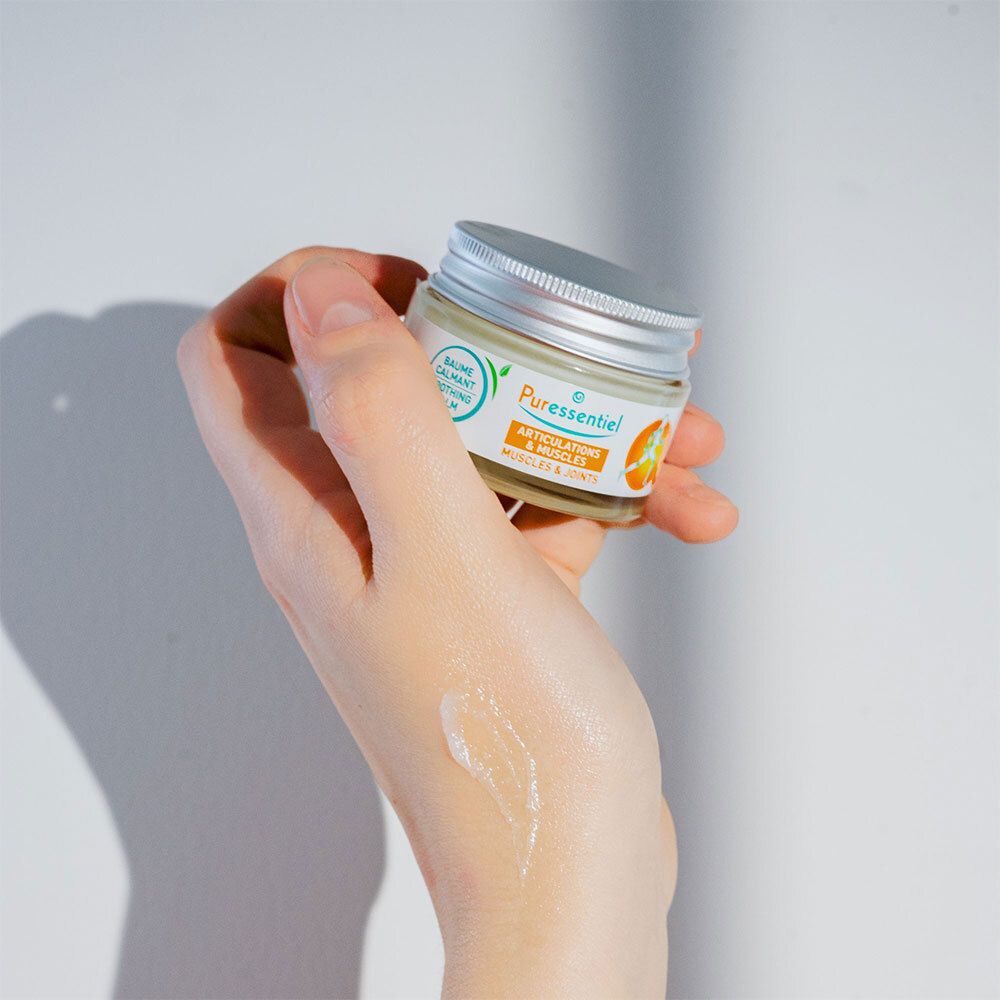 Hand met crème. Opschrift: Puressentiel, Spieren & Gewrichten, verzachtende balsem. 14 essentiële oliën.